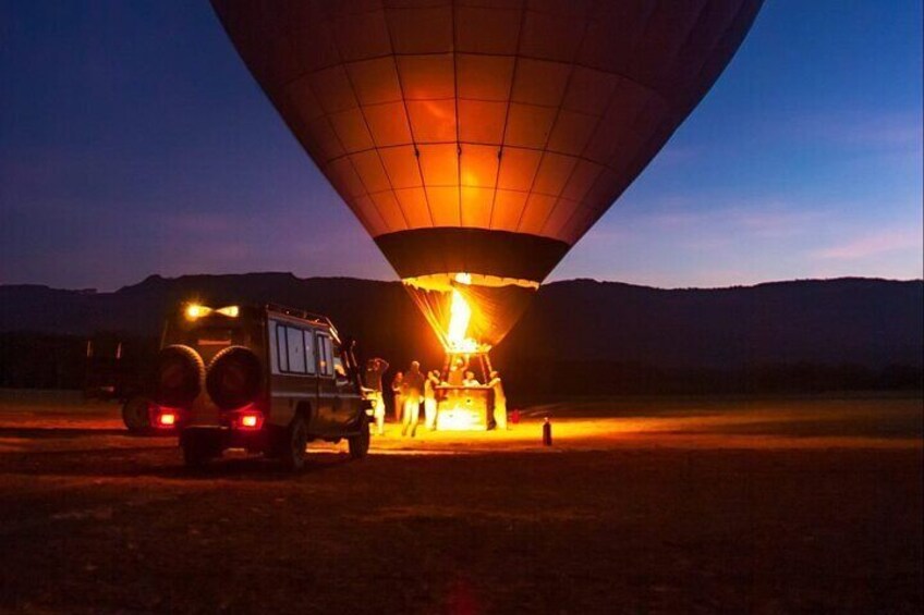 A hot air balloon being inflated at dusk with a vehicle nearby. 1