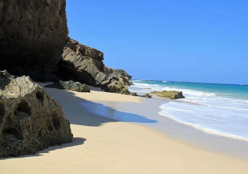 A sandy beach with a large rock formation and the ocean. 2