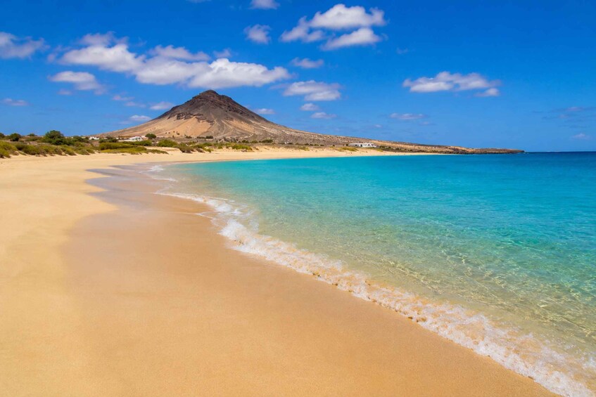 A beach with clear turquoise water, a sandy shore, and a mountain in the background. 3