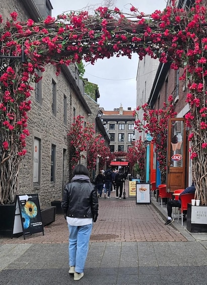 A pedestrian street with red flowers arching over the path, brick buildings, and outdoor seating at cafes. 3