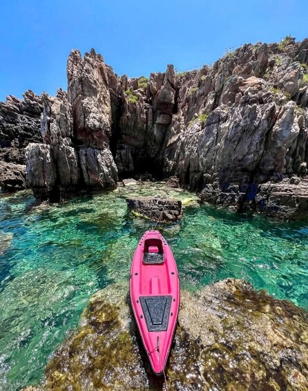 A pink kayak in clear water with rocky cliffs. 2