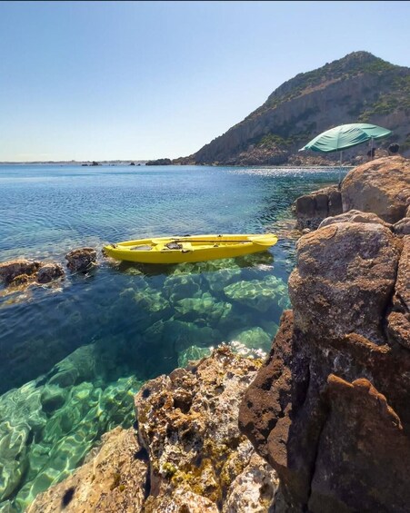 A yellow kayak on clear water with rocky shores and a green umbrella on a rock. 3