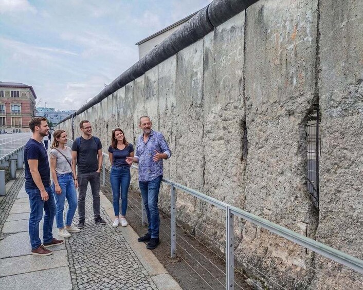 A group of people standing by a weathered stone wall with a metal railing, overlooking a cityscape. 2