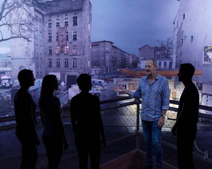 A man standing on a balcony overlooking a cityscape with buildings and a street. 1