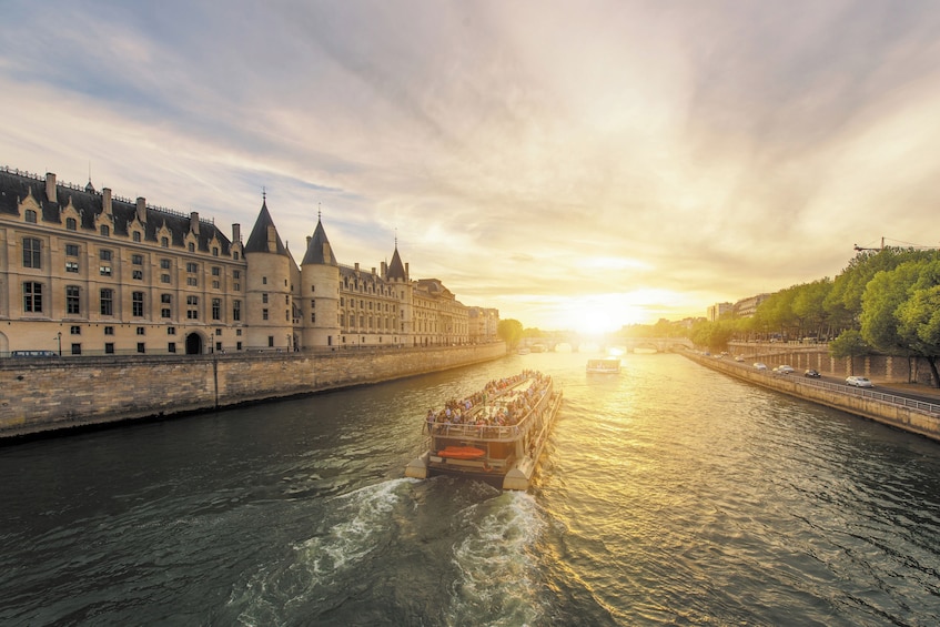 A river with a boat carrying passengers, a historic building on the left, and a sunset in the background. 2