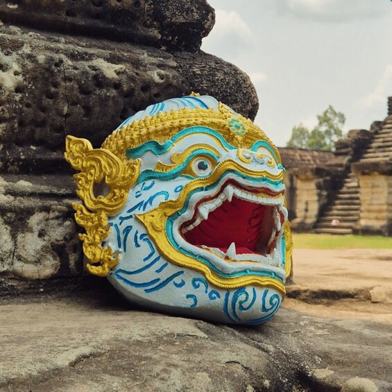 A colorful, intricately designed mask with a wide-open mouth, resting on a stone surface. 5