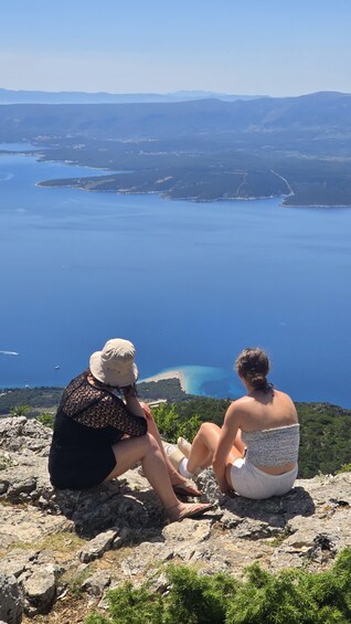 Two people sitting on a rocky outcrop overlooking a large body of water and distant mountains. 4
