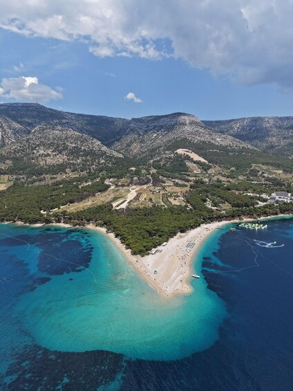 A coastal landscape with a beach, clear turquoise waters, and mountainous terrain. 1