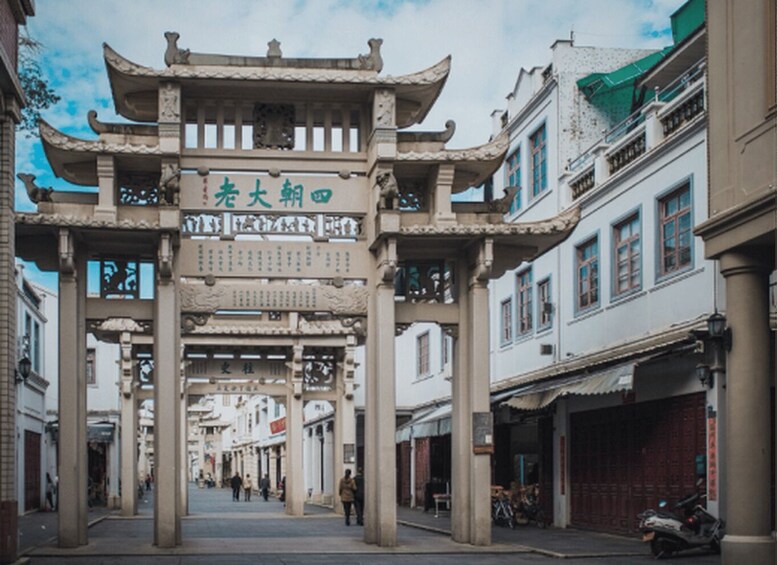 A traditional Chinese archway with characters, flanked by buildings with European-style windows and a clear sky. 1
