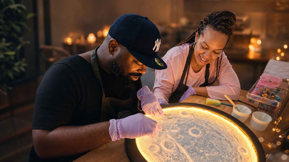 Two people working with a glowing, circular object, possibly a light installation, in a dimly lit indoor setting. 1