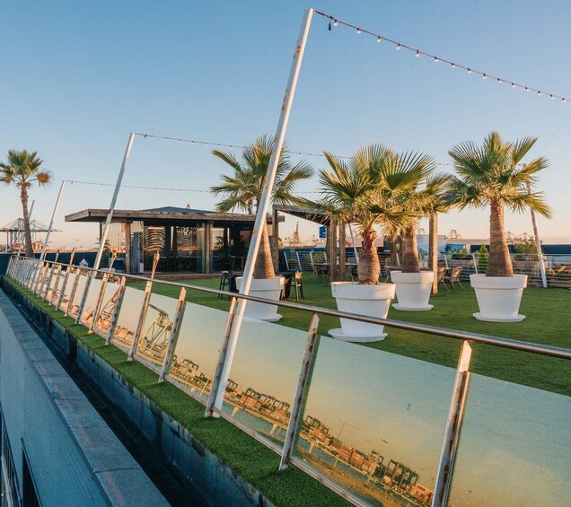 A waterfront promenade with palm trees, a covered seating area, and a view of the sea. 2