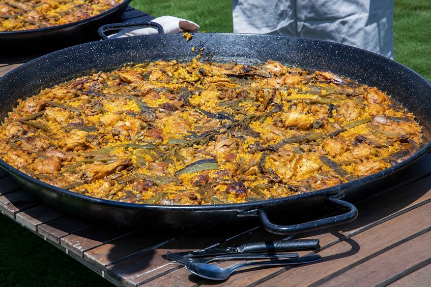 A large black pan filled with a yellow rice dish, possibly paella, with chicken and green beans, on an outdoor grill. 3