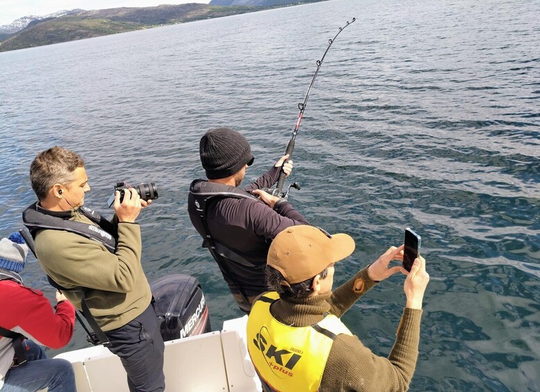 Three people on a boat, one taking photos, another fishing, and the third using a smartphone. 3