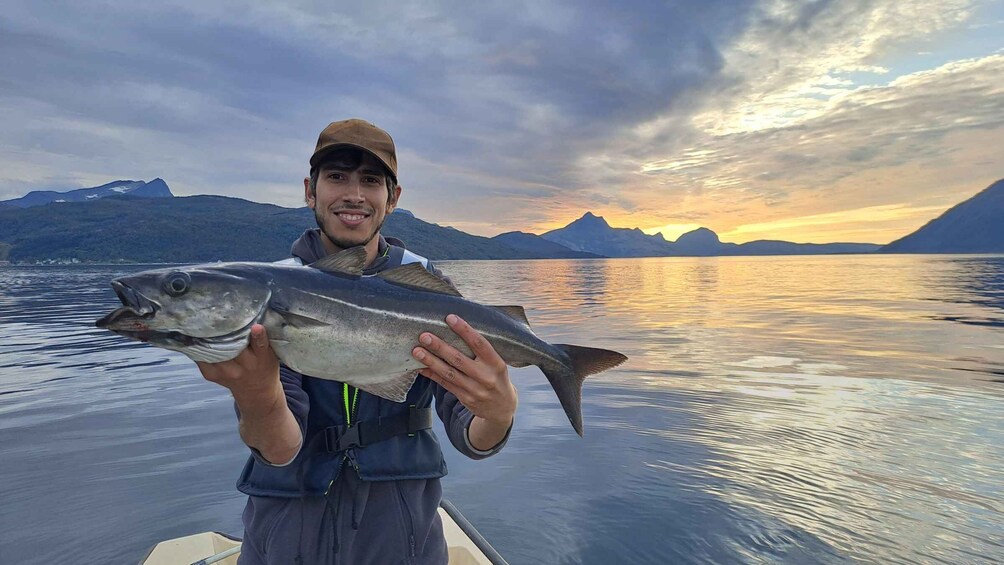 A person holding a fish on a boat with a mountainous landscape in the background. 2