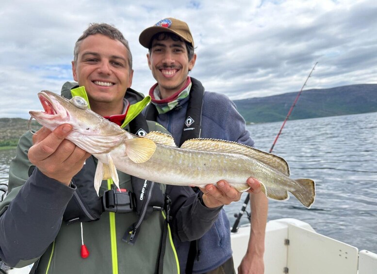 Two people holding a fish on a boat with a lake and mountains in the background. 4