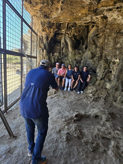 A group of people sitting inside a cave with rocky walls. 4