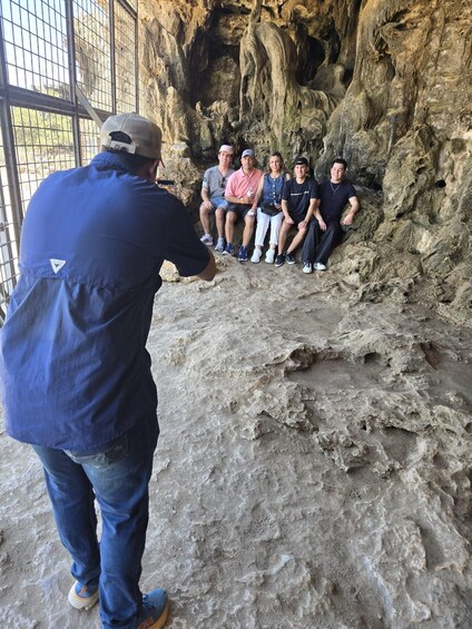 A group of people sitting on a rocky ledge inside a cave. 5
