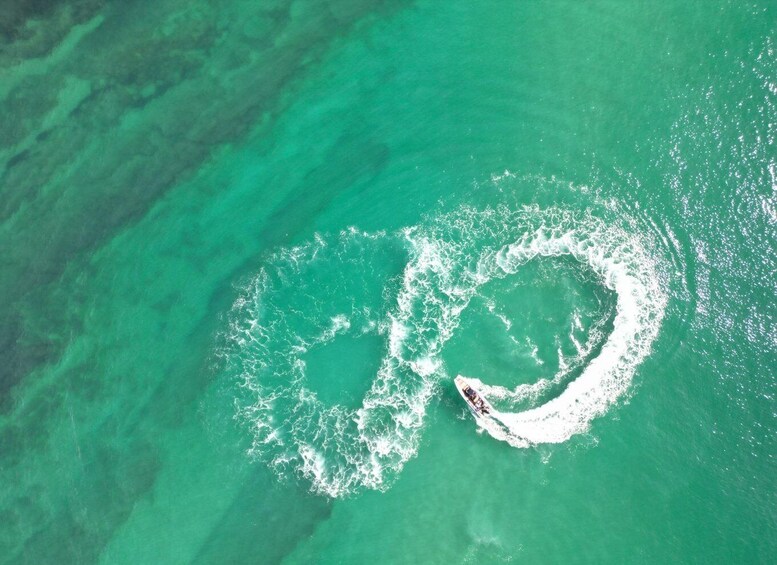 An aerial view of a circular whirlpool in turquoise waters with a boat creating a wake. 4
