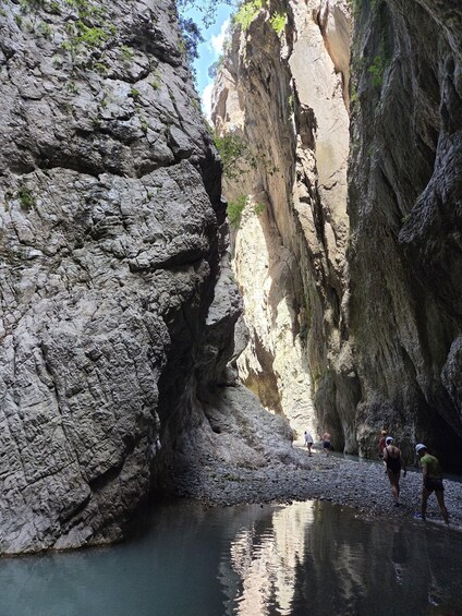 A rocky canyon with a narrow water stream and hikers. 1