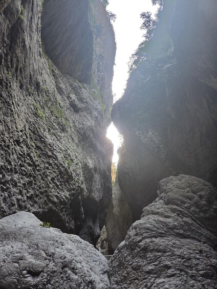 A narrow canyon with rugged rock walls and a visible light source at the top. 2