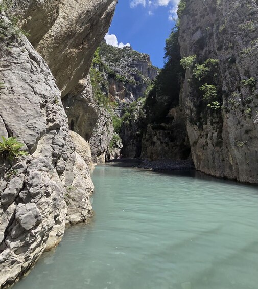A canyon with clear turquoise water, rocky cliffs, and sparse vegetation. 1