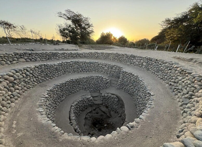 A spiral stone structure with a central hole, surrounded by a fence. 1