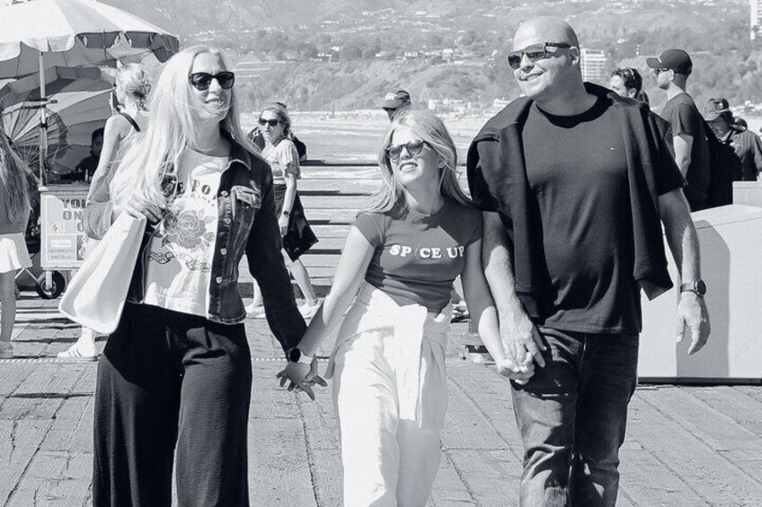 People walking on a paved path, holding hands, with a beach and ocean in the background. 3