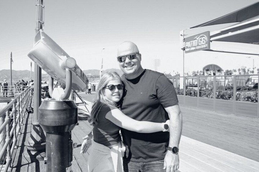 A man and a woman standing on a boardwalk with a large telescope and a sign for 'FANTASY 66' in the background. 5