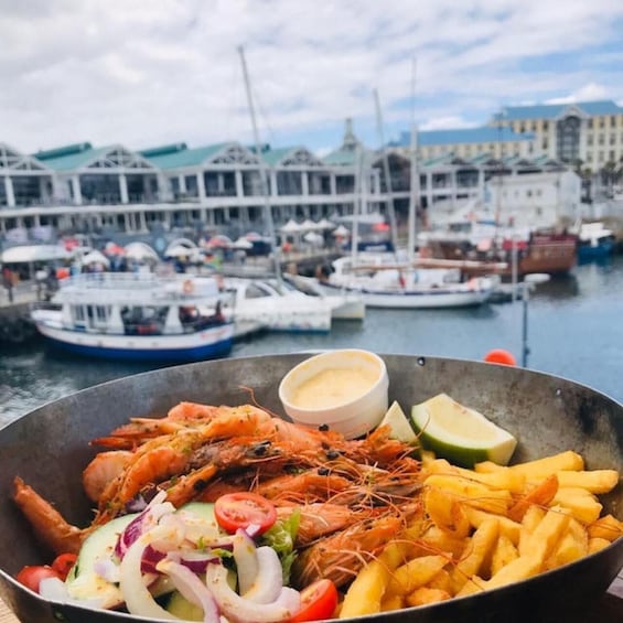 A seafood platter with shrimp, fries, and salad, with a marina and boats in the background. 1