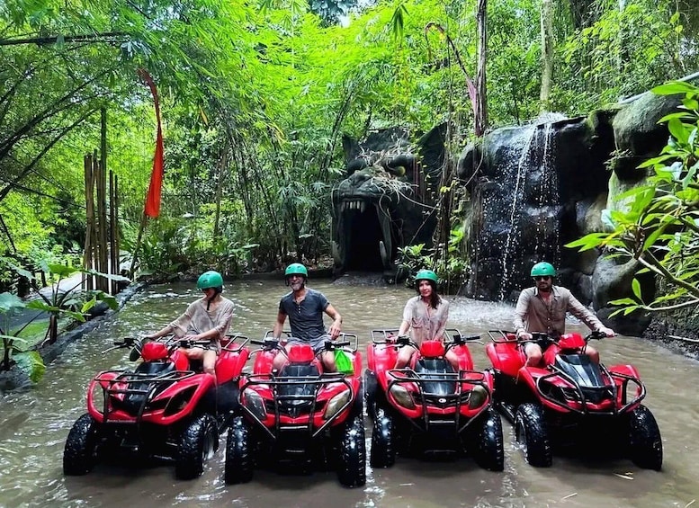 Four people on red all-terrain vehicles in a forested area with a waterfall. 3