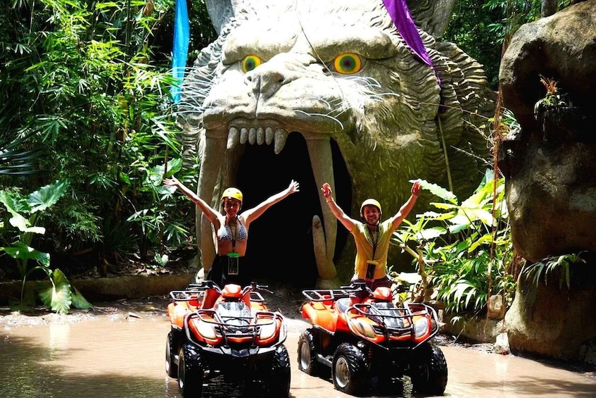 Two people on ATVs in front of a large, rocky, dragon-like structure. 5