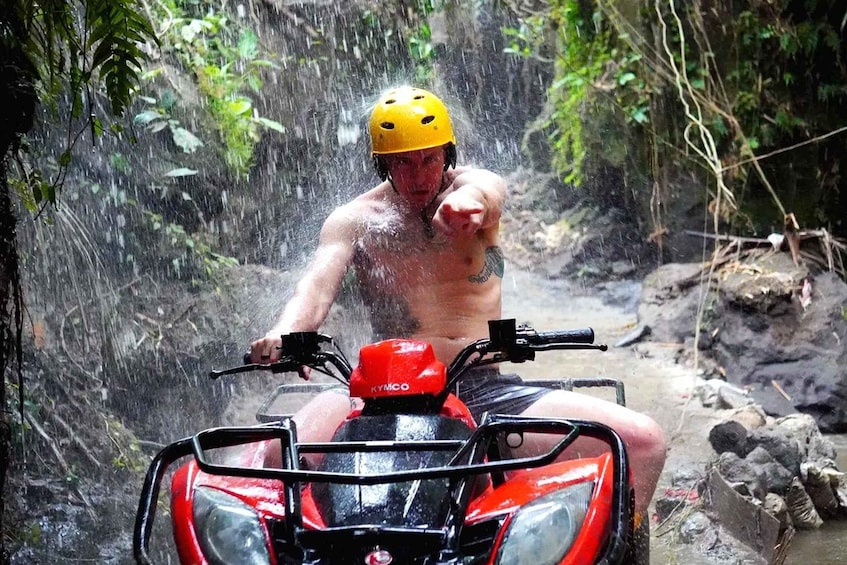 A person on a red ATV in a forested area with water cascading down. 1