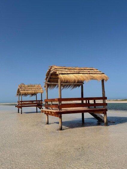 Two thatched beach huts on a sandy beach with clear blue skies. 1