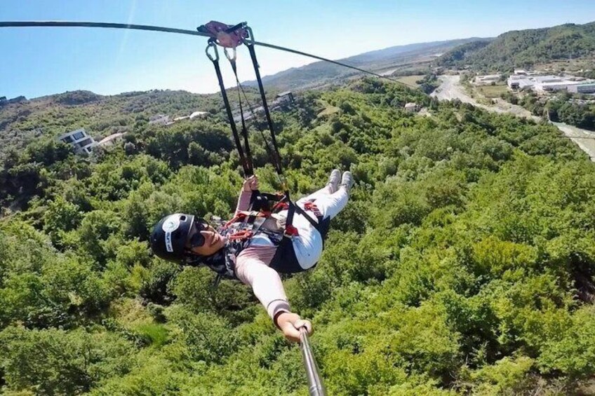 A person bungee jumping with a harness and helmet, suspended by a cable over a forested landscape. 5