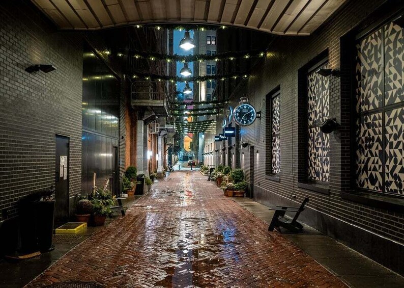 A wet cobblestone alley with hanging lights, a clock, and patterned walls. 4