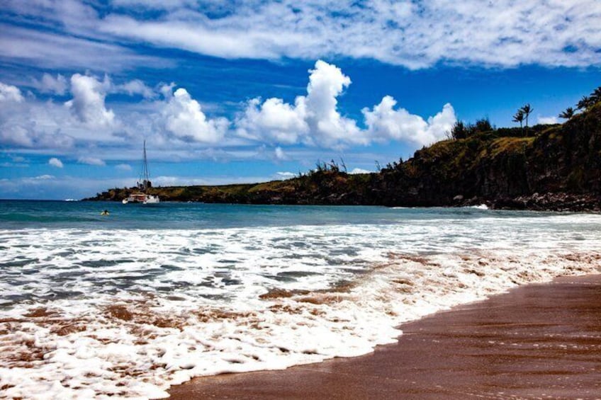 A beach with waves, a boat, and a rocky coastline. 5