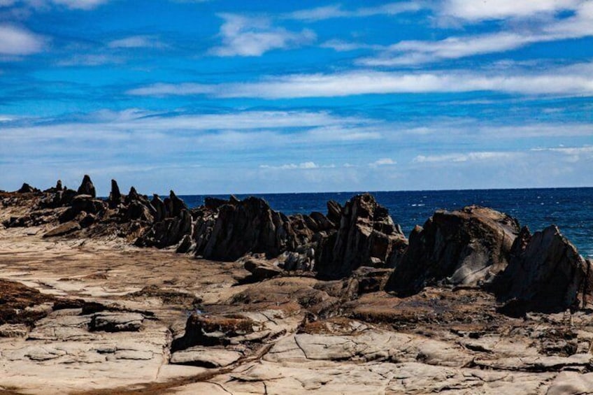 A rocky shoreline with jagged formations and a clear blue sky. 4