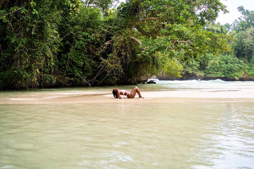 A person lying on a sandy beach with dense greenery and a river in the background. 2