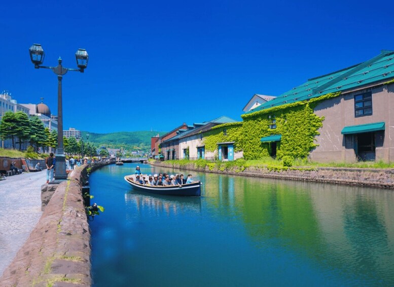A canal with a boat carrying passengers, buildings with green ivy, and a clear blue sky. 5