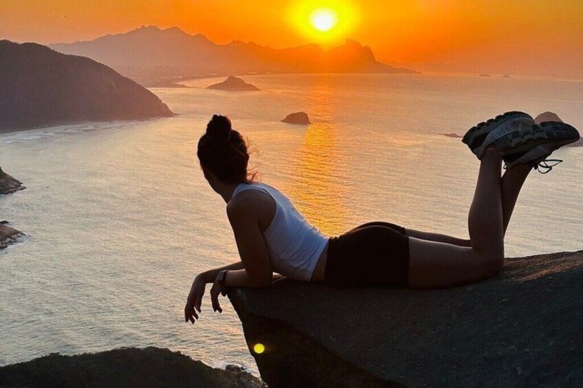 A person sitting on a cliff overlooking a body of water during sunset. 4