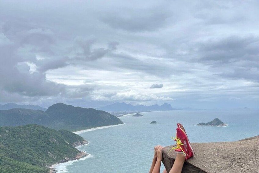 A person sitting on a cliff overlooking a coastline with mountains and the sea. 2
