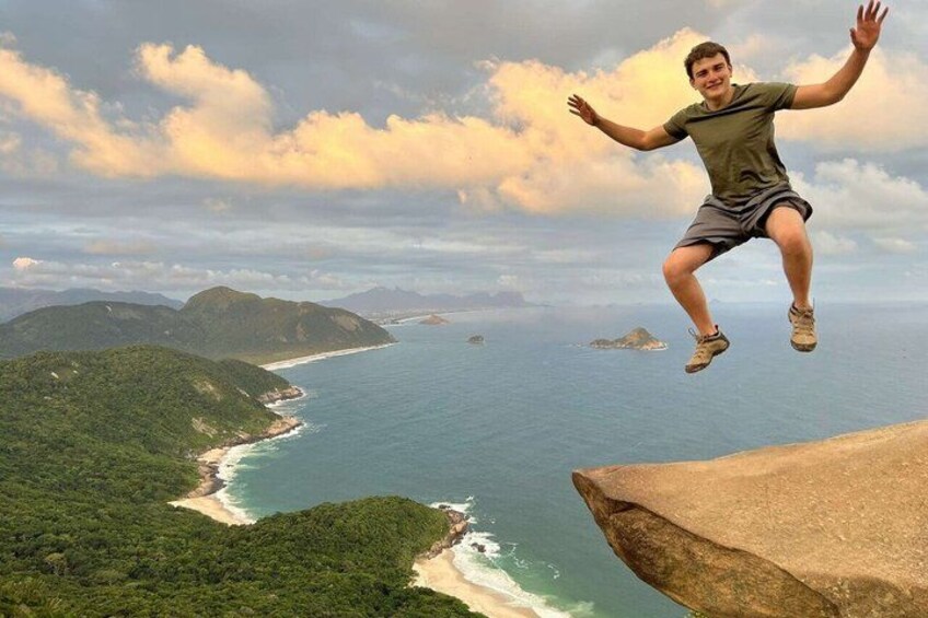 A person jumping off a cliff overlooking a coastal landscape with mountains and the ocean. 1