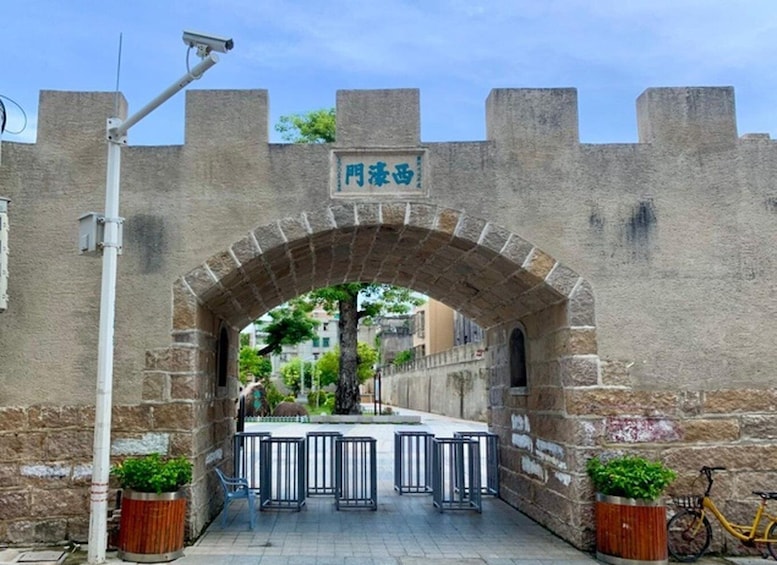 An arched stone gateway with a sign, potted plants, a bicycle, and a security camera. 5