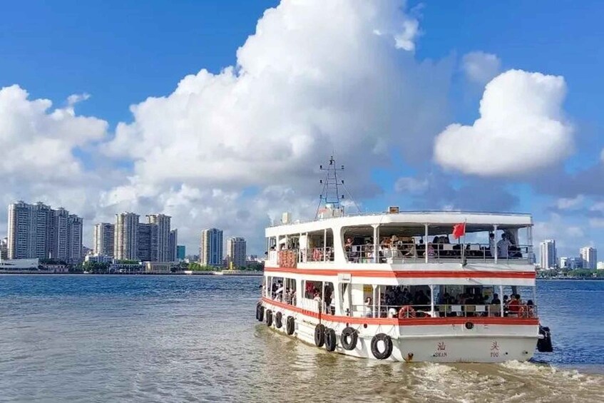 A white and red ferry with multiple decks, passengers, and a city skyline in the background. 1