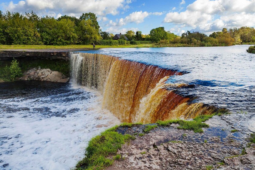 A waterfall cascading over rocks into a river, surrounded by greenery and a clear sky. 2