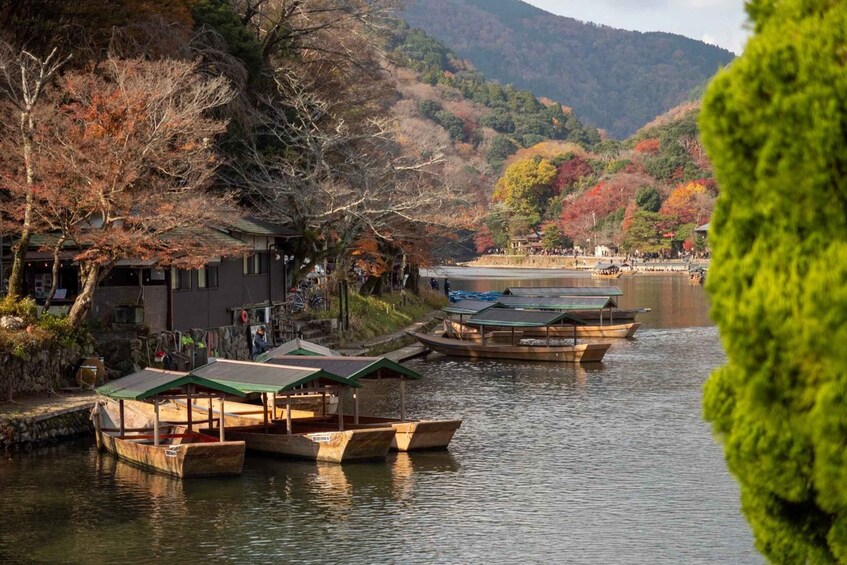 A calm river with wooden boats docked, surrounded by autumn-colored trees and a traditional building. 2