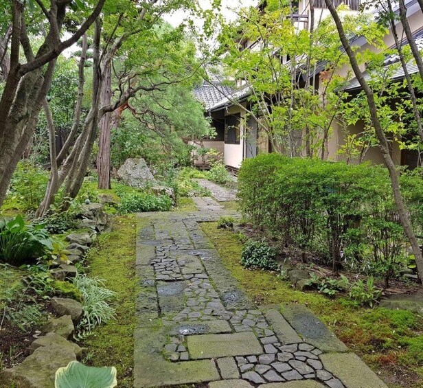 A stone pathway in a lush garden with trees and a traditional building. 2