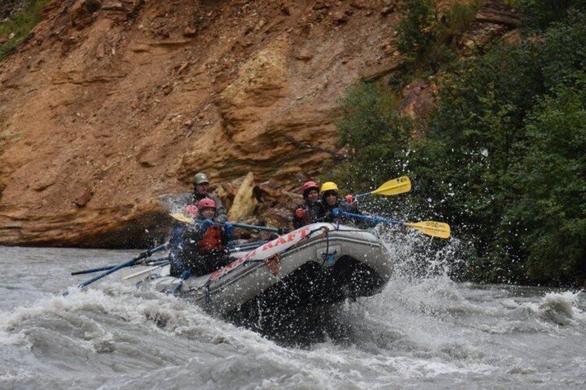 A white inflatable raft navigating turbulent waters with passengers and paddles. 1