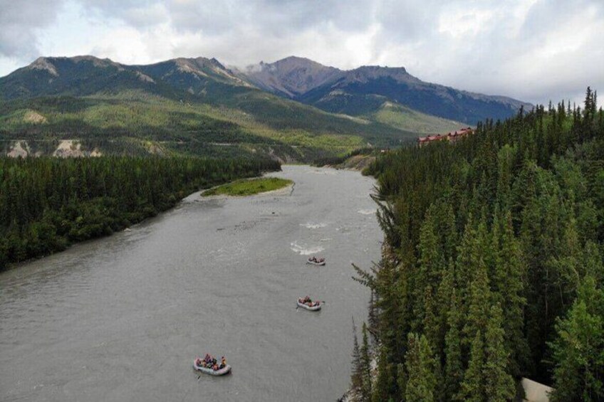 A river with three boats, surrounded by dense forest and mountains. 3