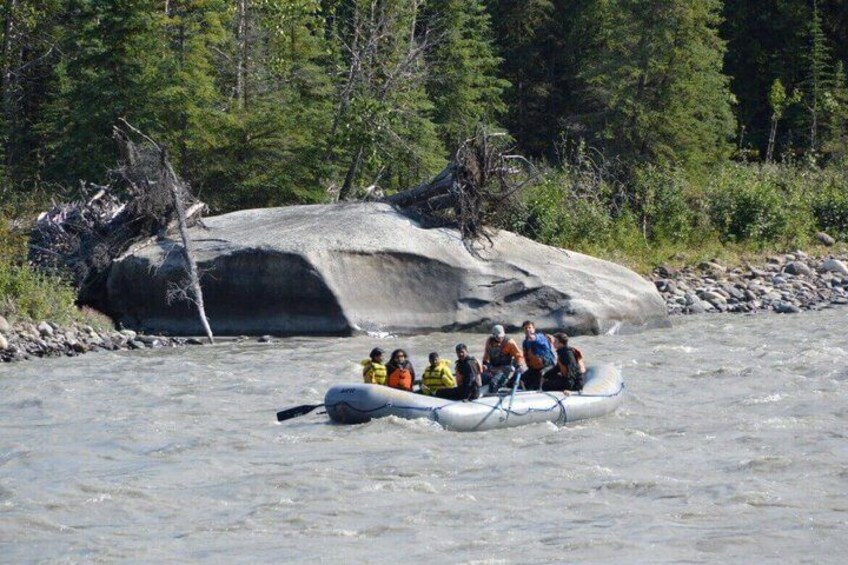 A group of people rafting on a river with a large rock in the background. 3